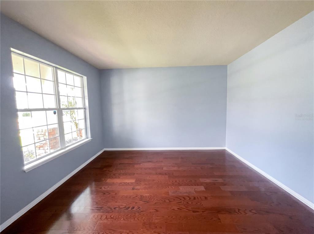 An empty room with light blue walls, a large window, and dark hardwood flooring — 15130 OVATION DRIVE, WINTER GARDEN, FL