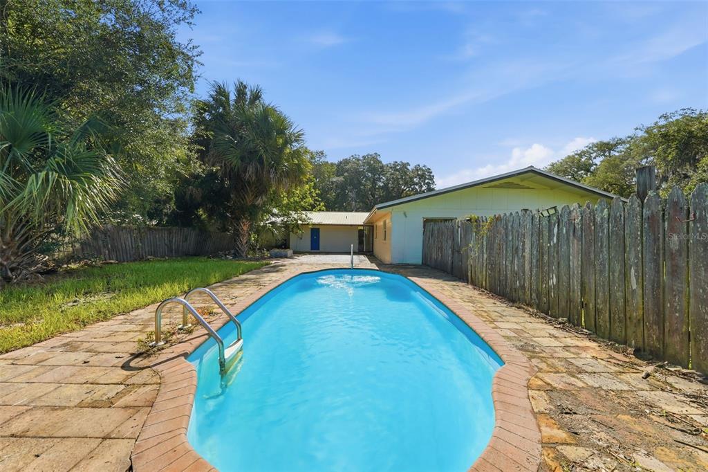 An outdoor swimming pool with a brick deck sits in a backyard with a wooden fence — 22526 SE 62ND AVENUE, HAWTHORNE, FL