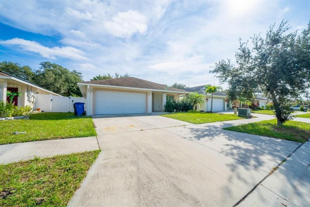 A single-story house with a white garage door and a concrete driveway under a blue sky — 2025 PEACEFUL PALM STREET, RUSKIN, FL