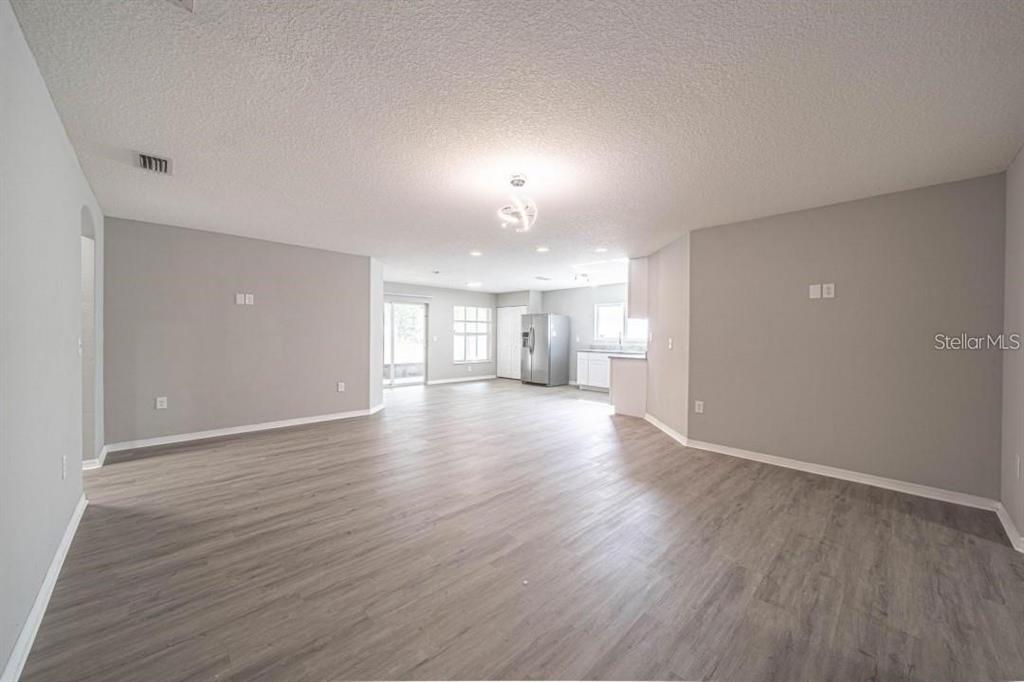 An open-concept living and dining area features light gray walls and wood-look laminate flooring — 2025 PEACEFUL PALM STREET, RUSKIN, FL