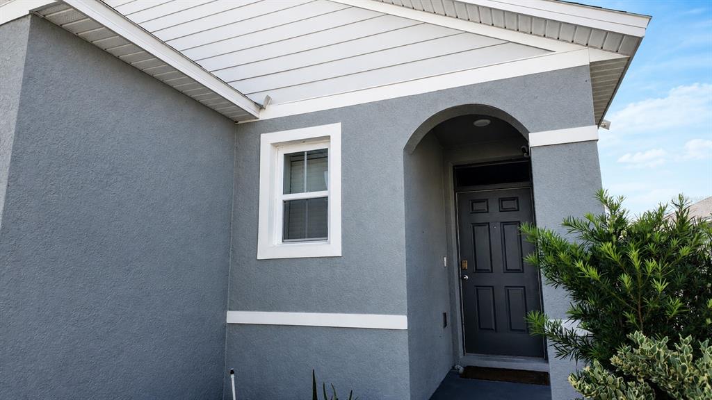 The exterior of a gray stucco house features a white-trimmed window and a dark door — 1032 ANDEAN LANE, DAVENPORT, FL