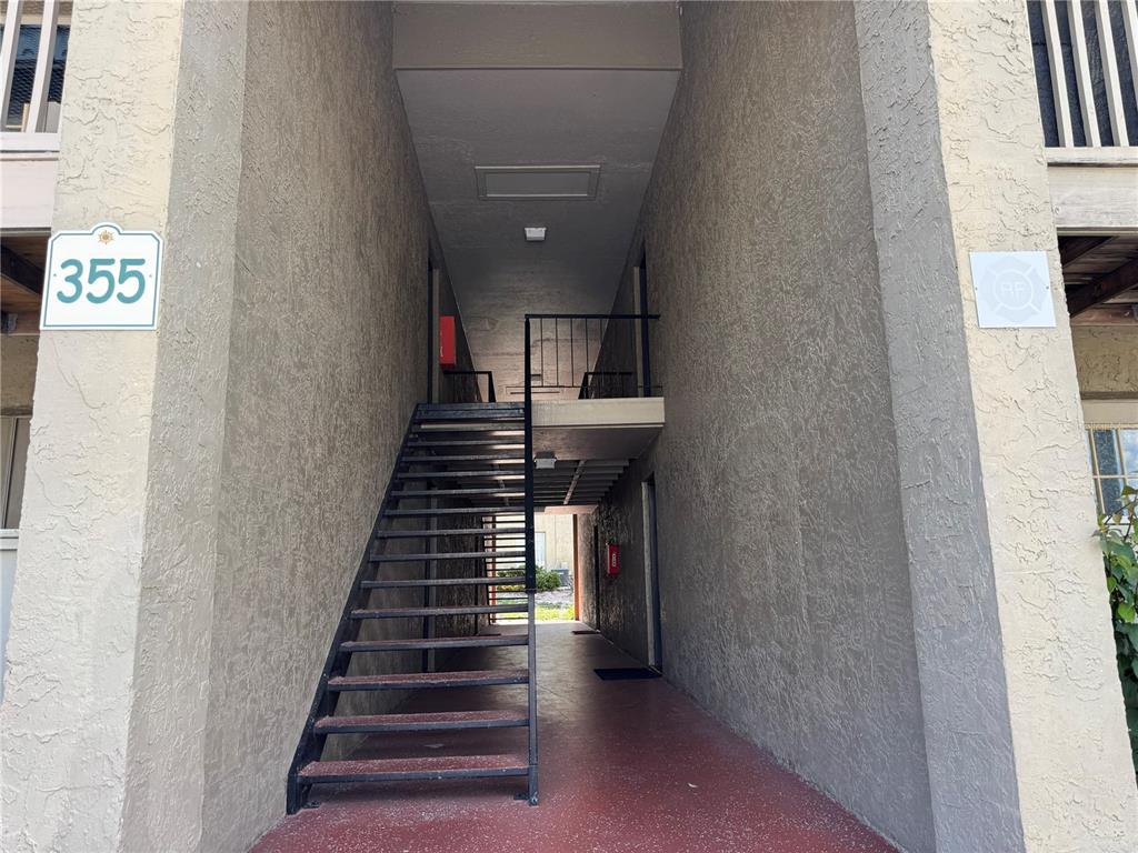 An outdoor staircase leads to an upper-level walkway between two stucco apartment building walls — 355 WYMORE ROAD UNIT 202, ALTAMONTE SPRINGS, FL