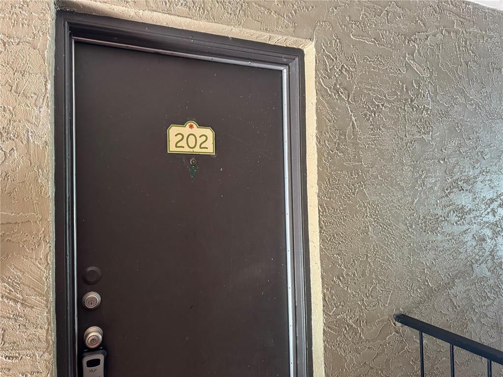 A brown apartment door with the number 202 is set into a textured tan wall — 355 WYMORE ROAD UNIT 202, ALTAMONTE SPRINGS, FL