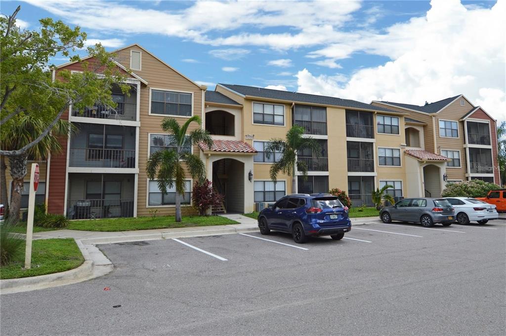 A multi-story apartment building with tan siding and screened balconies sits behind a parking lot — 11901 4TH STREET N UNIT 9105, ST PETERSBURG, FL