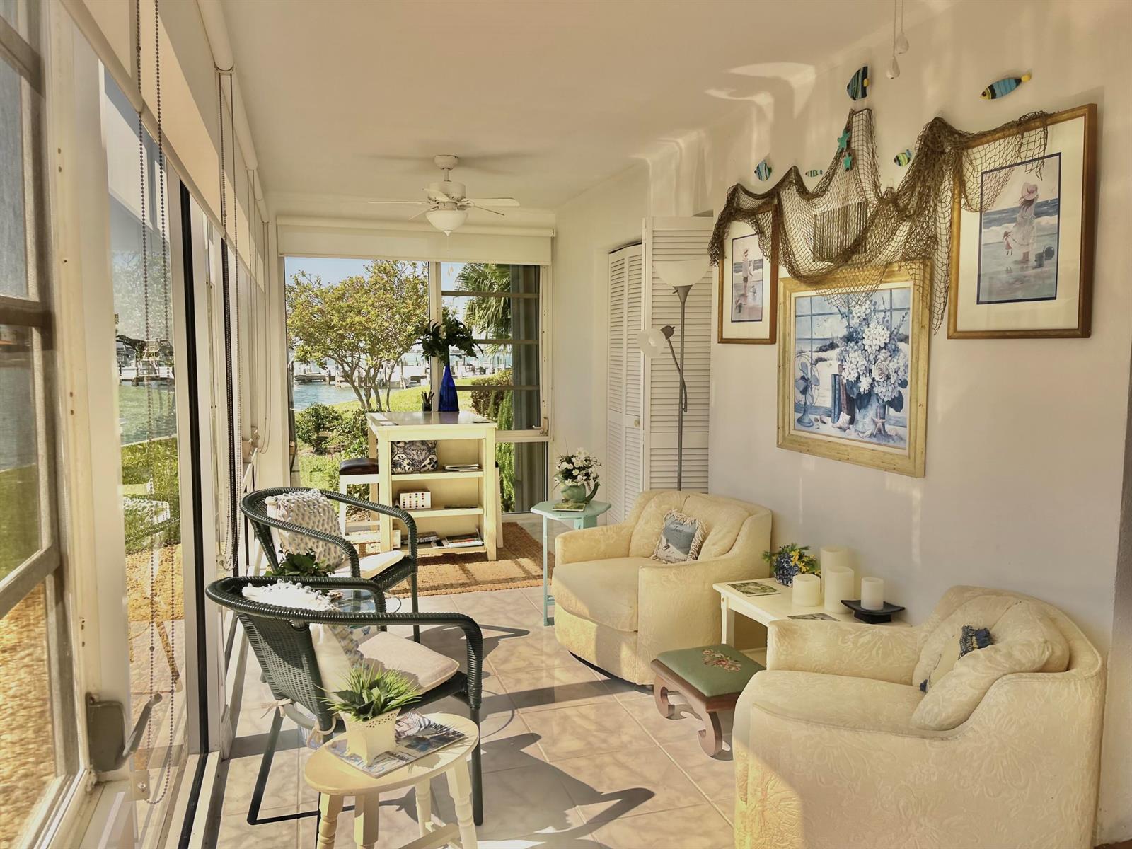 A sunroom features wicker chairs, cream armchairs, nautical wall decor, and a view of water — 1351 Bayshore Drive # 108, Fort Pierce FL 34949, FORT PIERCE, FL