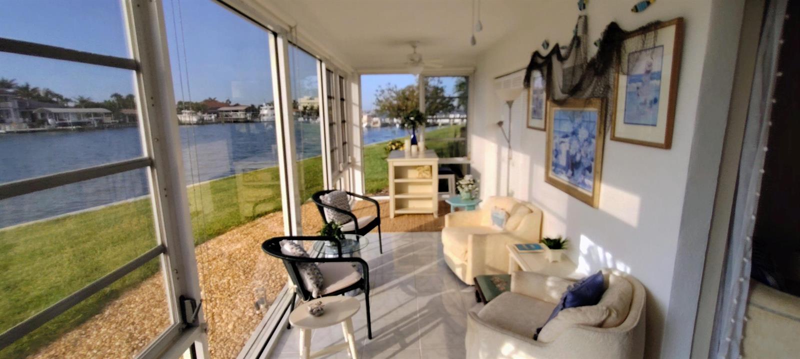 A sunroom with tile floors, comfortable seating, and large windows overlooking a canal and lawn — 1351 Bayshore Drive # 108, Fort Pierce FL 34949, FORT PIERCE, FL