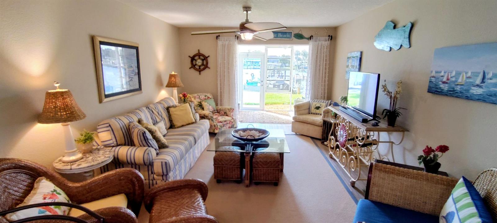 A coastal-themed living room features a striped sofa, wicker chairs, and a glass coffee table — 1351 Bayshore Drive # 108, Fort Pierce FL 34949, FORT PIERCE, FL