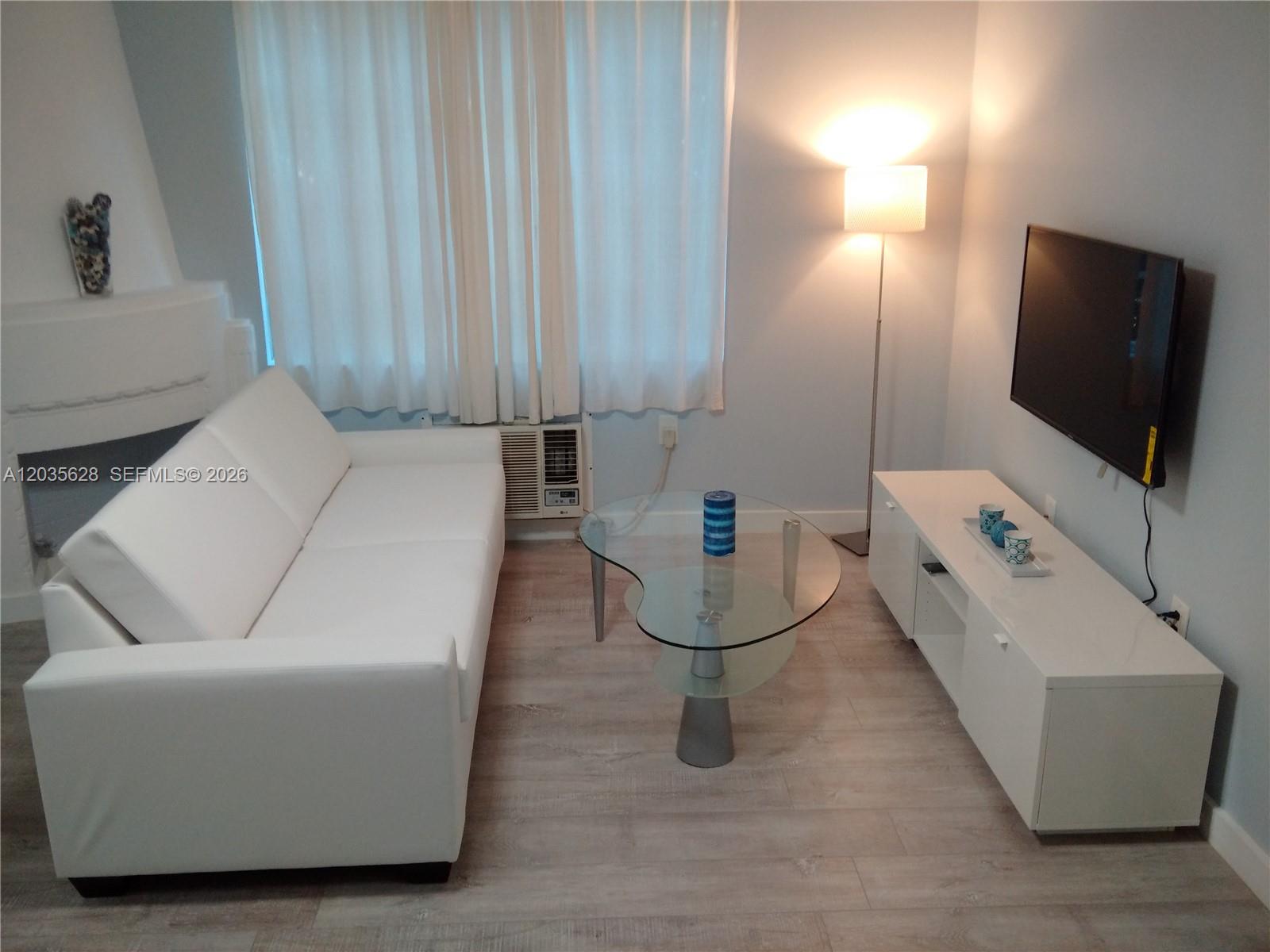 A living room features a white sofa, glass coffee table, media console, and wall-mounted television — 1525 Meridian Ave # 104, Miami Beach FL 33139, MIAMI BEACH, FL