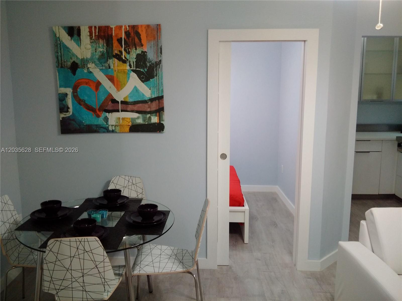 A dining area with a glass table and abstract art leads into a small bedroom — 1525 Meridian Ave # 104, Miami Beach FL 33139, MIAMI BEACH, FL