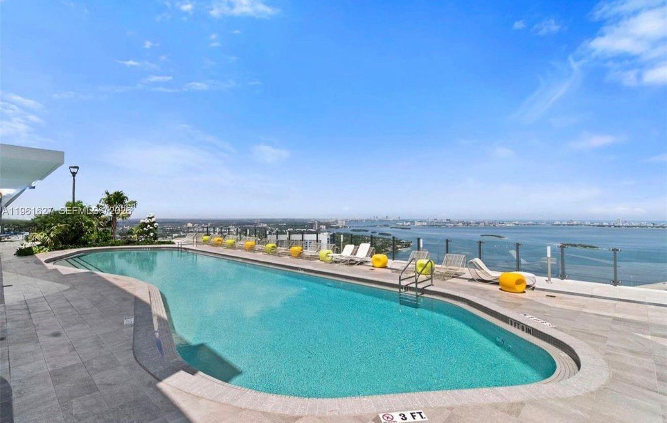 An outdoor rooftop swimming pool overlooks a bay with a city skyline in the distance — 501 NE 31st St # 1808, Miami FL 33137, MIAMI, FL