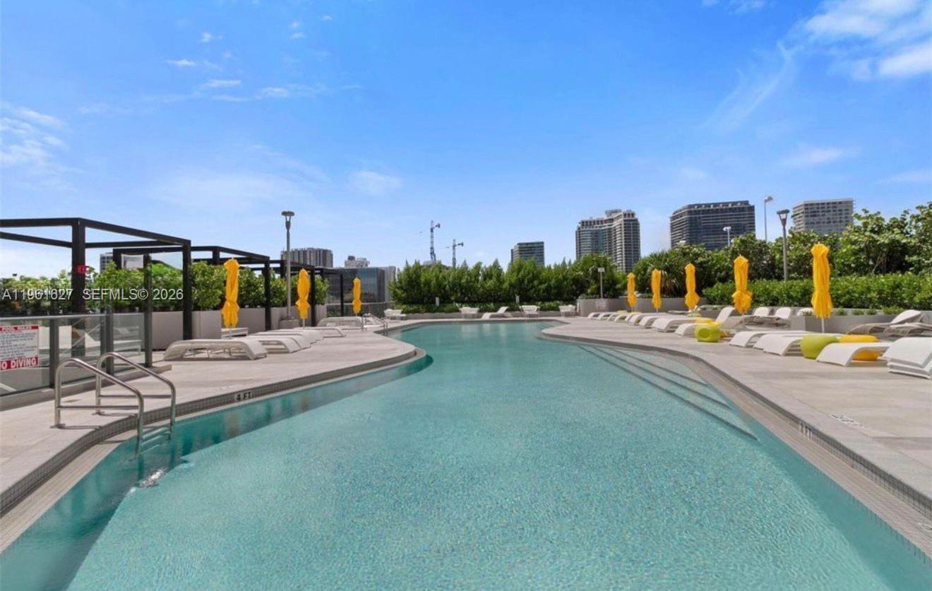 An outdoor swimming pool with lounge chairs and yellow umbrellas on a sunny day — 501 NE 31st St # 1808, Miami FL 33137, MIAMI, FL