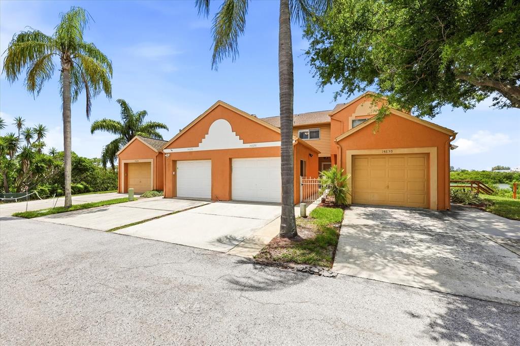 An exterior view of a multi-unit orange building with four garage doors and palm trees — 14628 LORIDAWN DRIVE UNIT 13, SEMINOLE, FL