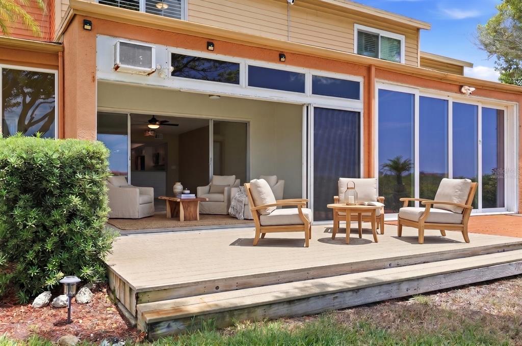 A wooden deck features outdoor seating in front of a house with large sliding glass doors — 14628 LORIDAWN DRIVE UNIT 13, SEMINOLE, FL