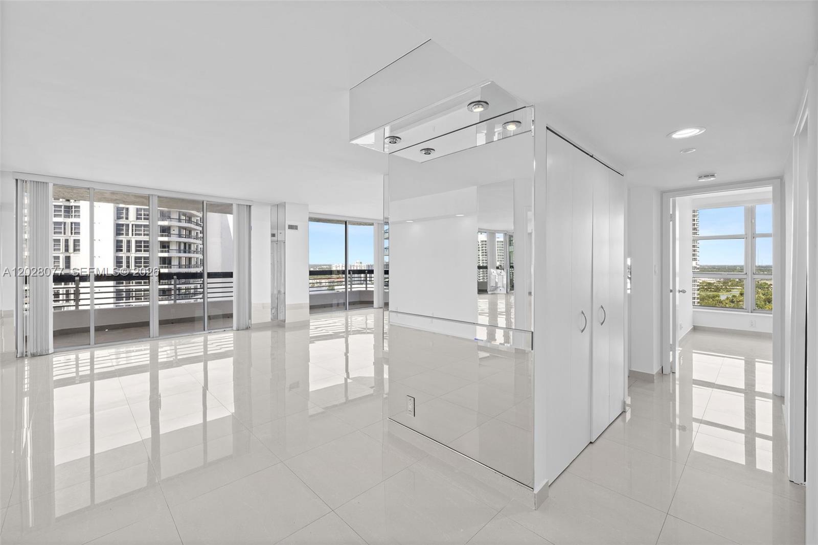 A bright, empty room features white tile floors, a mirrored pillar, and floor-to-ceiling windows — 19195 NE 36th Ct # 2705, Aventura FL 33180, AVENTURA, FL