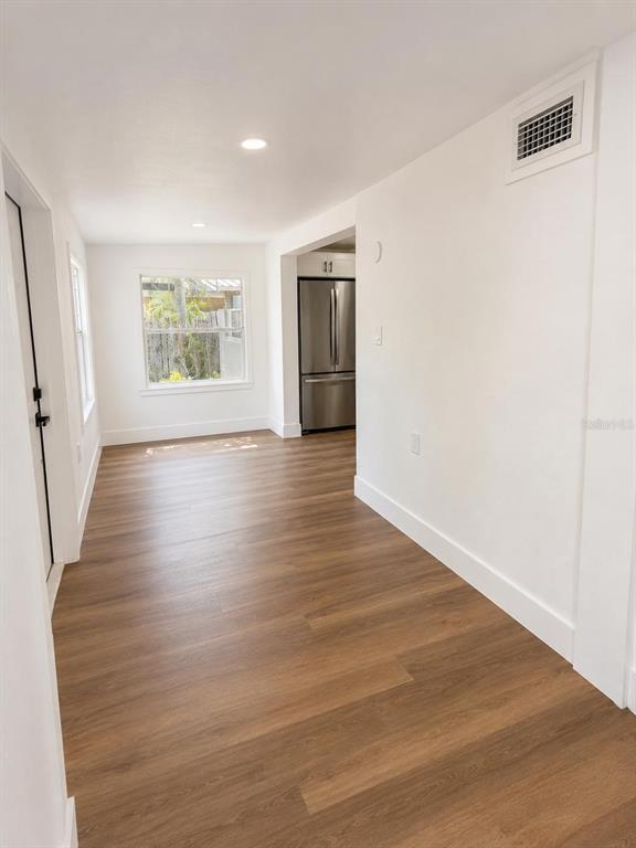 A bright room with wood-look flooring leads to a kitchen featuring a stainless steel refrigerator — 7211 JAMES STREET, PORT RICHEY, FL