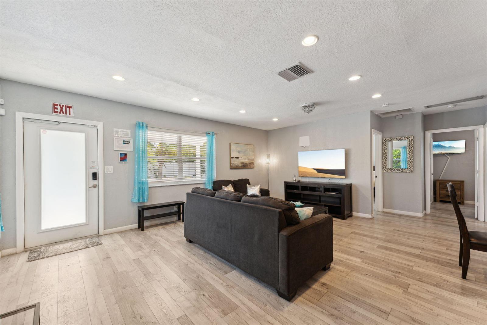 A living room features light wood-look flooring, a dark sofa, and a wall-mounted television — 1631 N Andrews Square, Fort Lauderdale FL 33311, FORT LAUDERDALE, FL