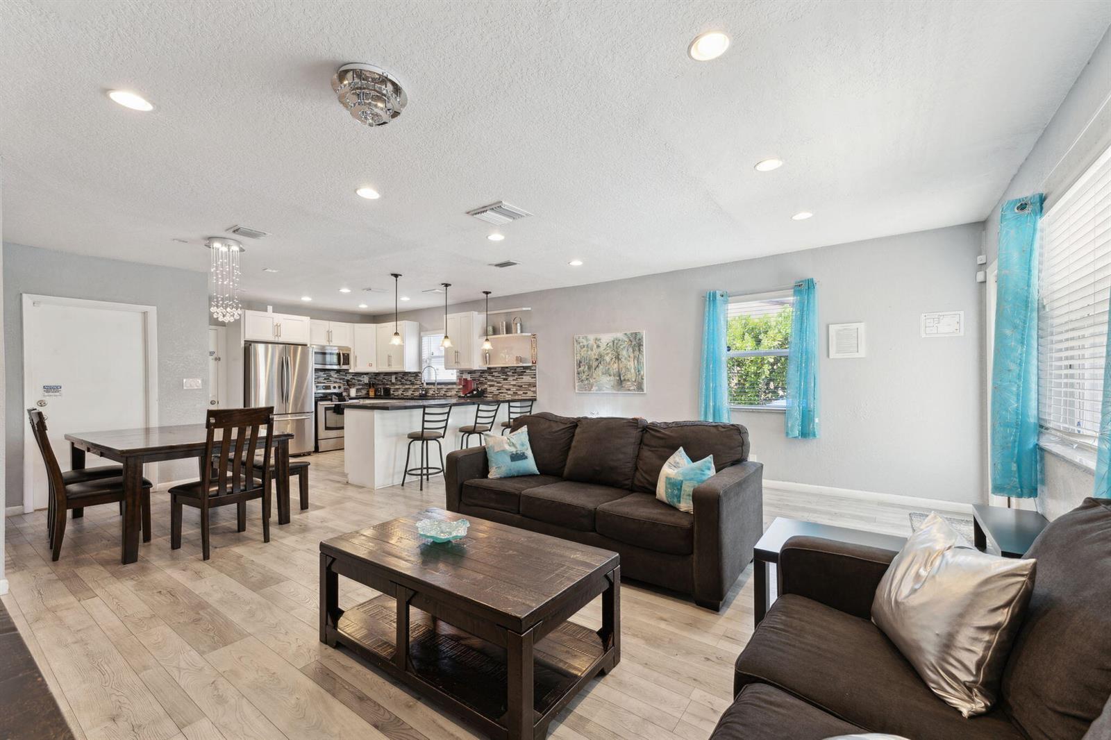 An open-concept living room and kitchen featuring dark furniture, light wood-look flooring, and blue curtains — 1631 N Andrews Square, Fort Lauderdale FL 33311, FORT LAUDERDALE, FL