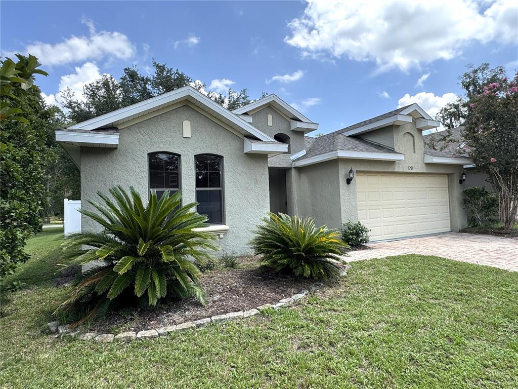 A single-story stucco house with a two-car garage and two prominent sago palms in front — 1209 BRAMLEY LANE, DELAND, FL