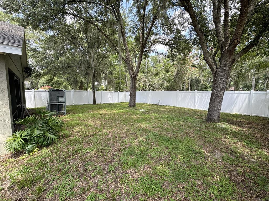 A grassy backyard features mature trees, a white vinyl fence, and a screened-in porch area — 1209 BRAMLEY LANE, DELAND, FL