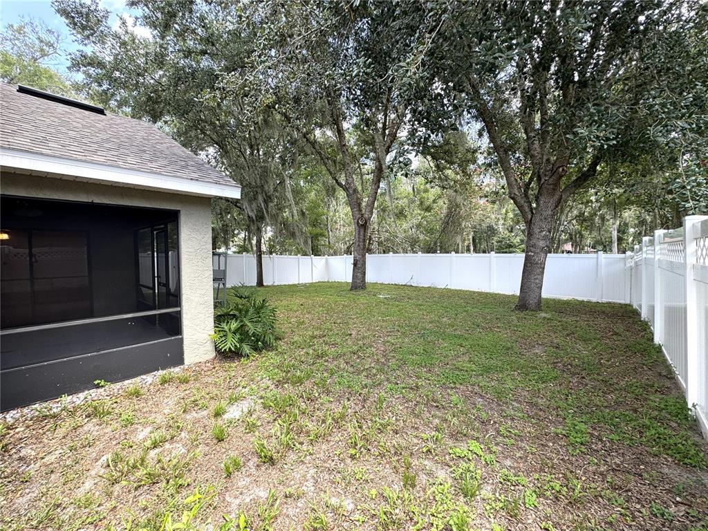 A backyard features a screened-in patio, mature trees, and a white vinyl privacy fence — 1209 BRAMLEY LANE, DELAND, FL