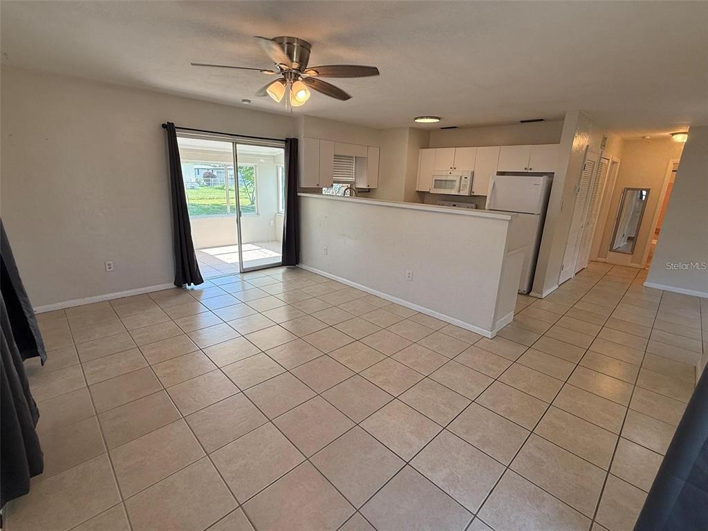 An open-concept living area features tile flooring, a kitchen with white cabinets, and sliding doors — 22180 MIDWAY BOULEVARD, PORT CHARLOTTE, FL