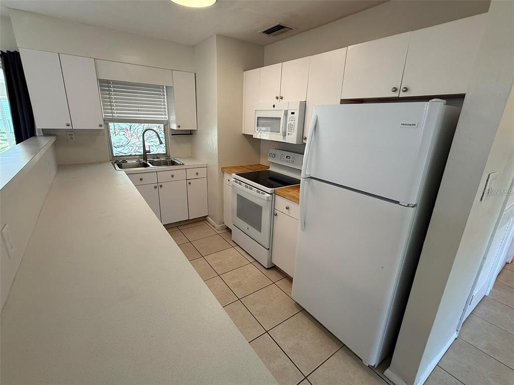 A kitchen features white cabinets, white appliances, a double sink, and light-colored tile flooring — 22180 MIDWAY BOULEVARD, PORT CHARLOTTE, FL