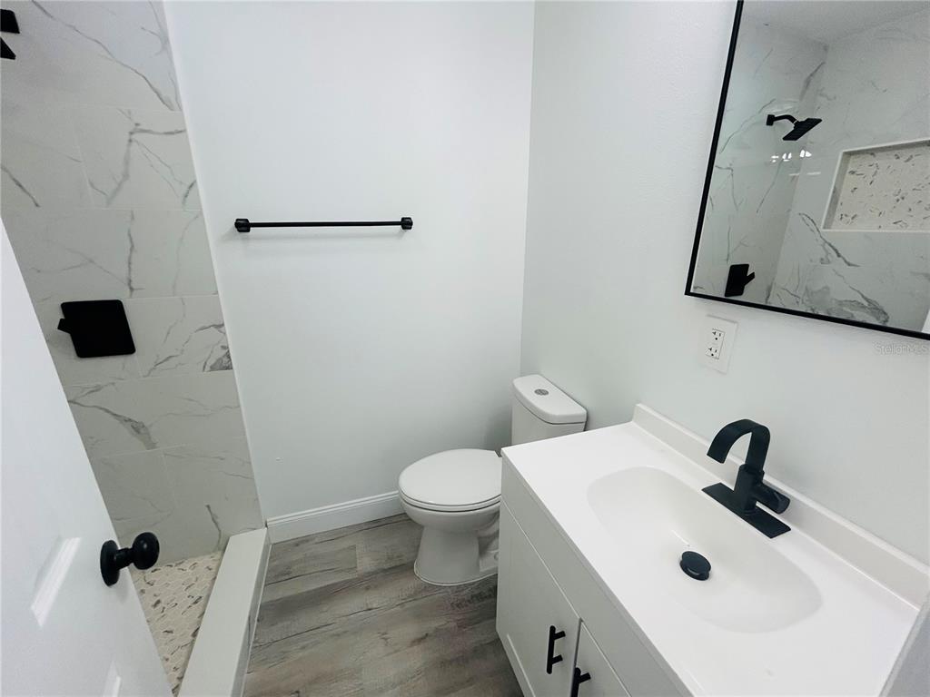 A bathroom features a white vanity, a toilet, and a walk-in shower with marble-look tile — 6603 COCOS DRIVE, ORLANDO, FL