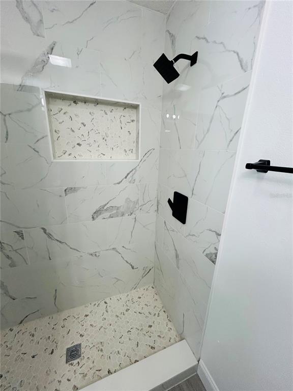A walk-in shower features white marble-look wall tiles, a pebble floor, and black fixtures — 6603 COCOS DRIVE, ORLANDO, FL