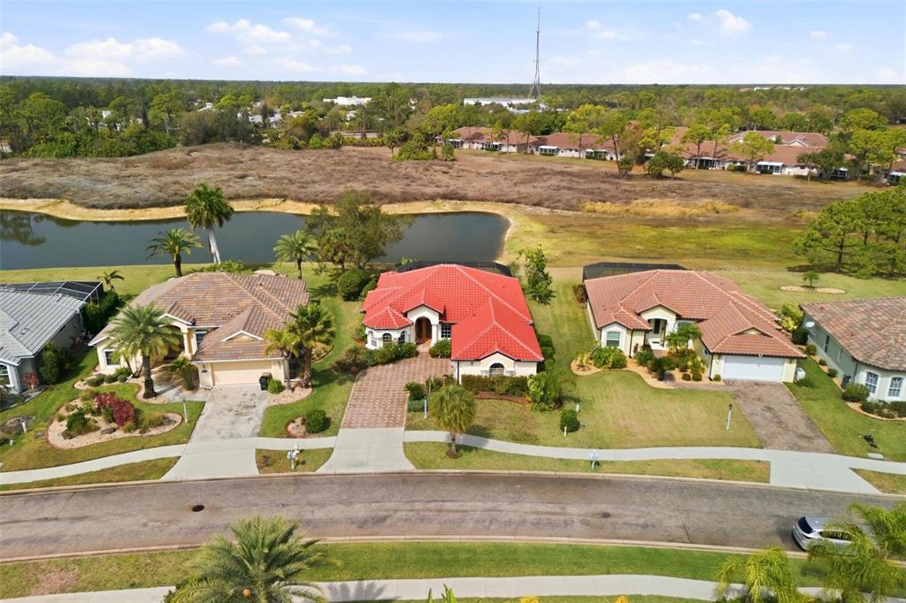 An aerial view shows three suburban houses with tiled roofs situated along a curved street — 2499 SILVER PALM ROAD, NORTH PORT, FL