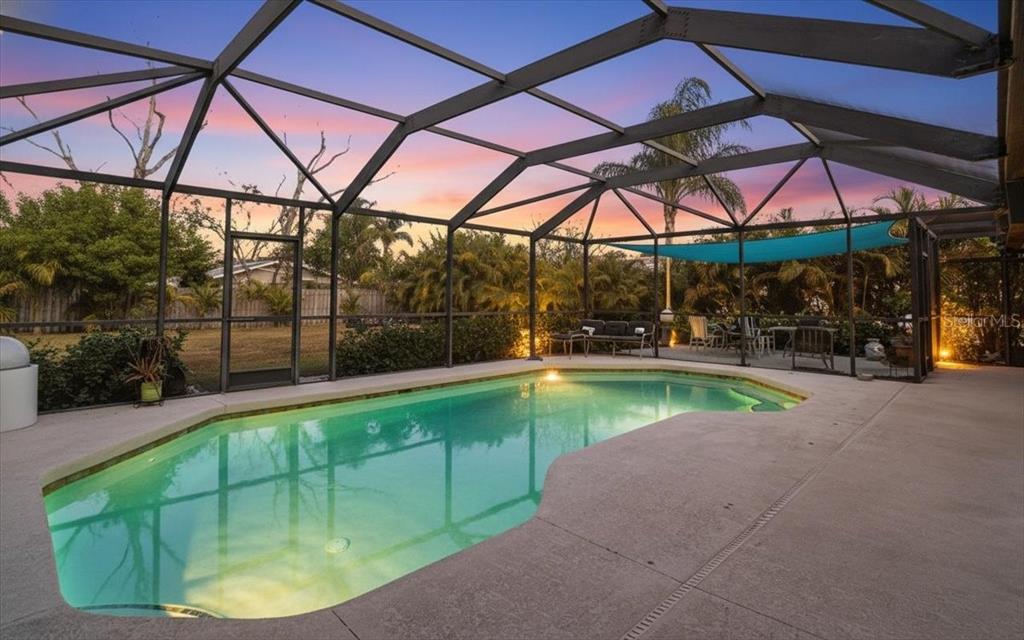 A screened-in patio features a swimming pool and outdoor seating under a sunset sky — 1606 4TH STREET W, PALMETTO, FL