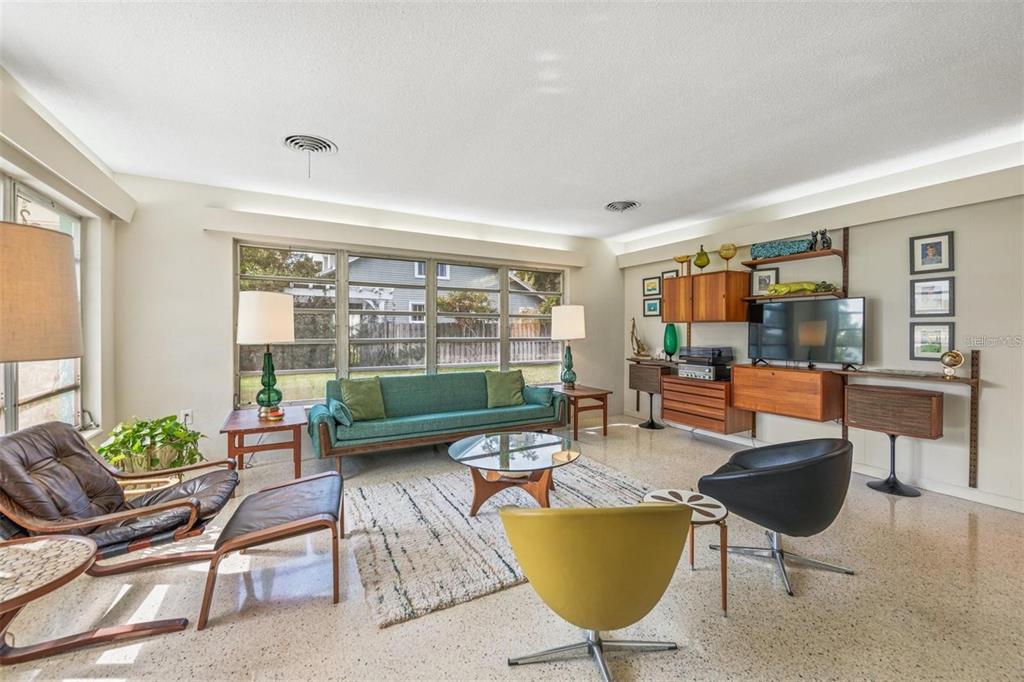 A mid-century modern living room features a teal sofa, wood shelving, and terrazzo flooring — 1606 4TH STREET W, PALMETTO, FL