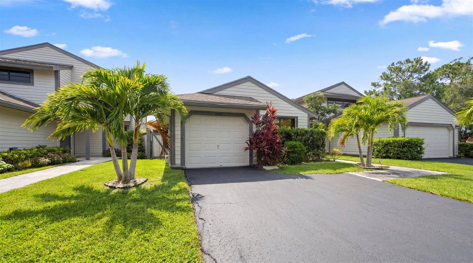 A residential property exterior features two garage doors, palm trees, and a paved driveway — 2482 Bedford Mews Drive, Wellington FL 33414, WELLINGTON, FL