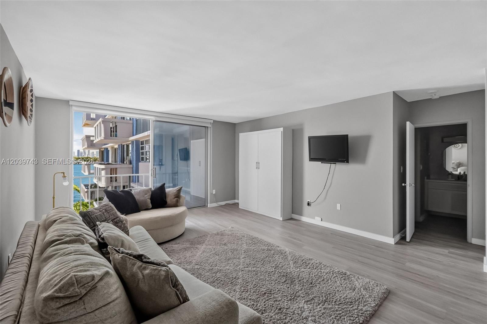 A living room features light wood flooring, a gray sofa, a circular chair, and a balcony — 800 West Ave # 533, Miami Beach FL 33139, MIAMI BEACH, FL