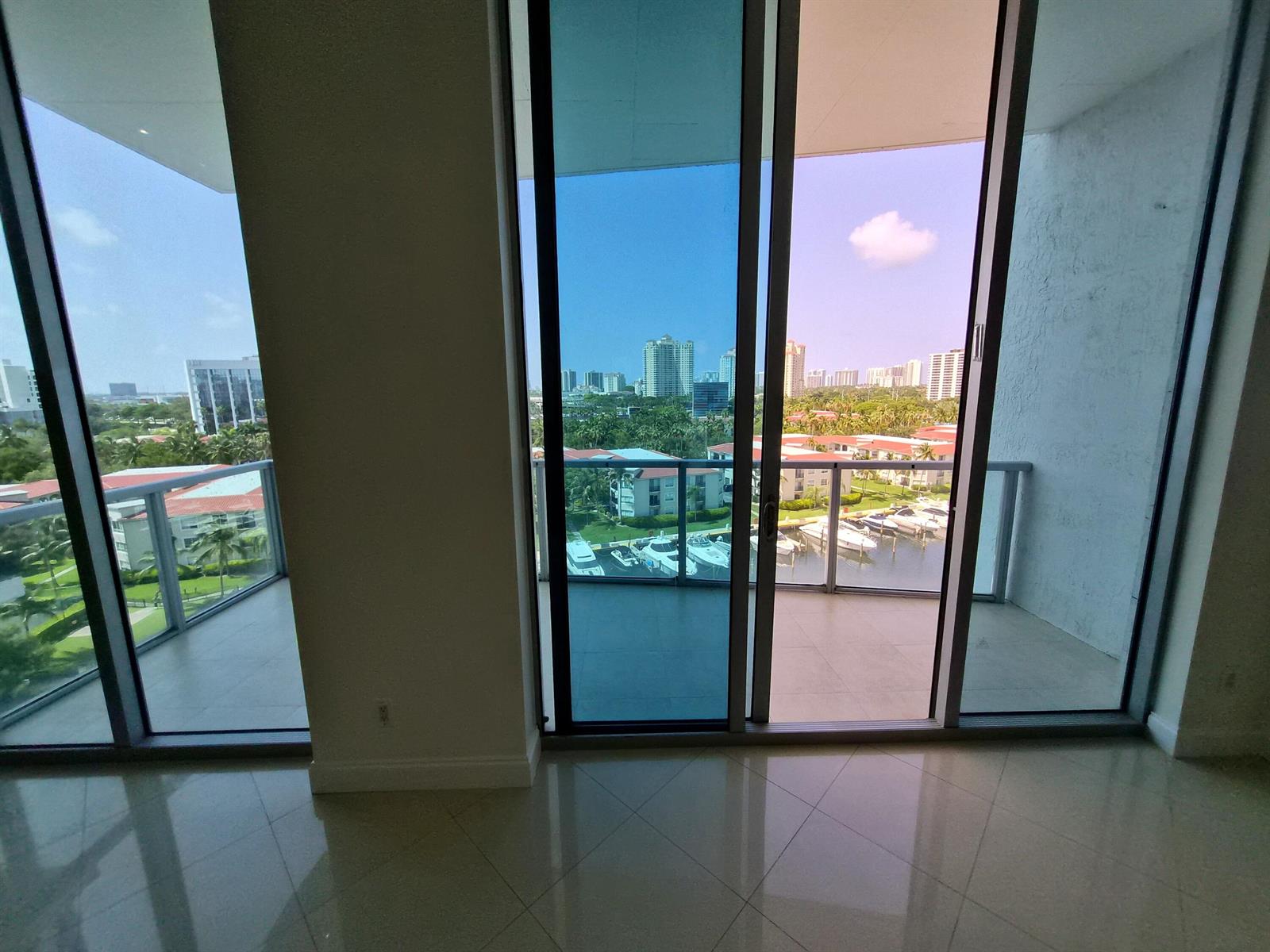 A room with light tile flooring features floor-to-ceiling glass doors overlooking a marina and city — 3029 NE 188th Street, Aventura FL 33180, AVENTURA, FL