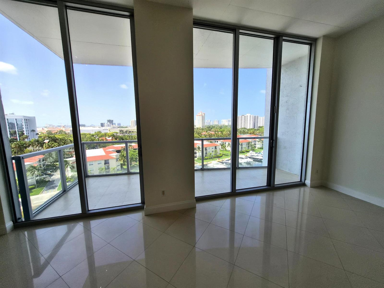 An empty room with large glass sliding doors, tiled floors, and a balcony overlooking buildings — 3029 NE 188th Street, Aventura FL 33180, AVENTURA, FL