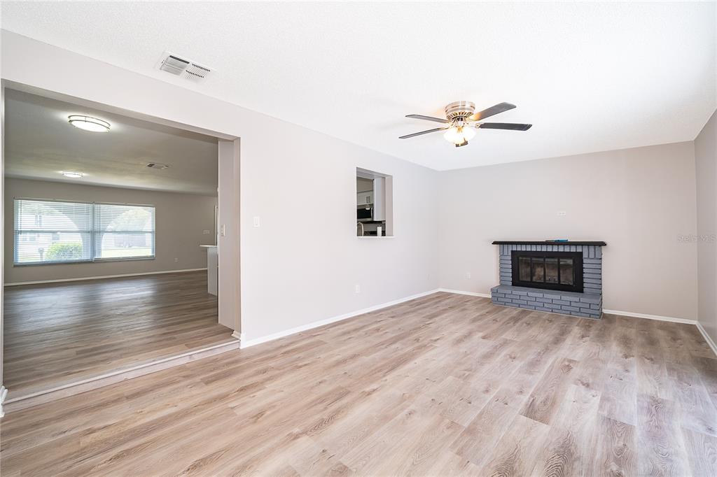 A living room with light wood-look flooring, a gray brick fireplace, and a ceiling fan — 8448 MATTITUCK CIRCLE, ORLANDO, FL