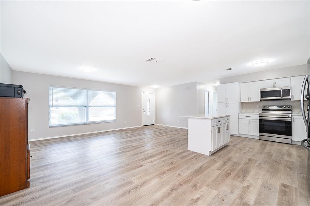 An open-concept living area features light wood-look flooring, white kitchen cabinets, and a center island — 8448 MATTITUCK CIRCLE, ORLANDO, FL