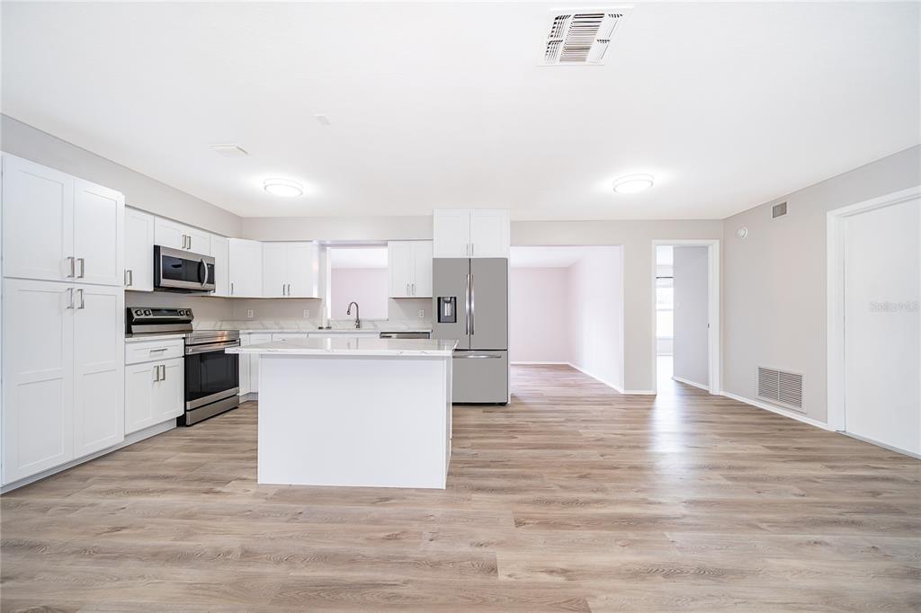 A modern kitchen features white cabinets, stainless steel appliances, a center island, and wood flooring — 8448 MATTITUCK CIRCLE, ORLANDO, FL