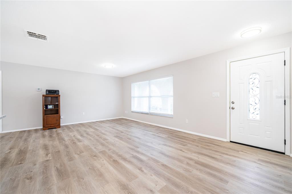 A bright living room features light wood-look flooring, neutral walls, a window with blinds, and a door — 8448 MATTITUCK CIRCLE, ORLANDO, FL