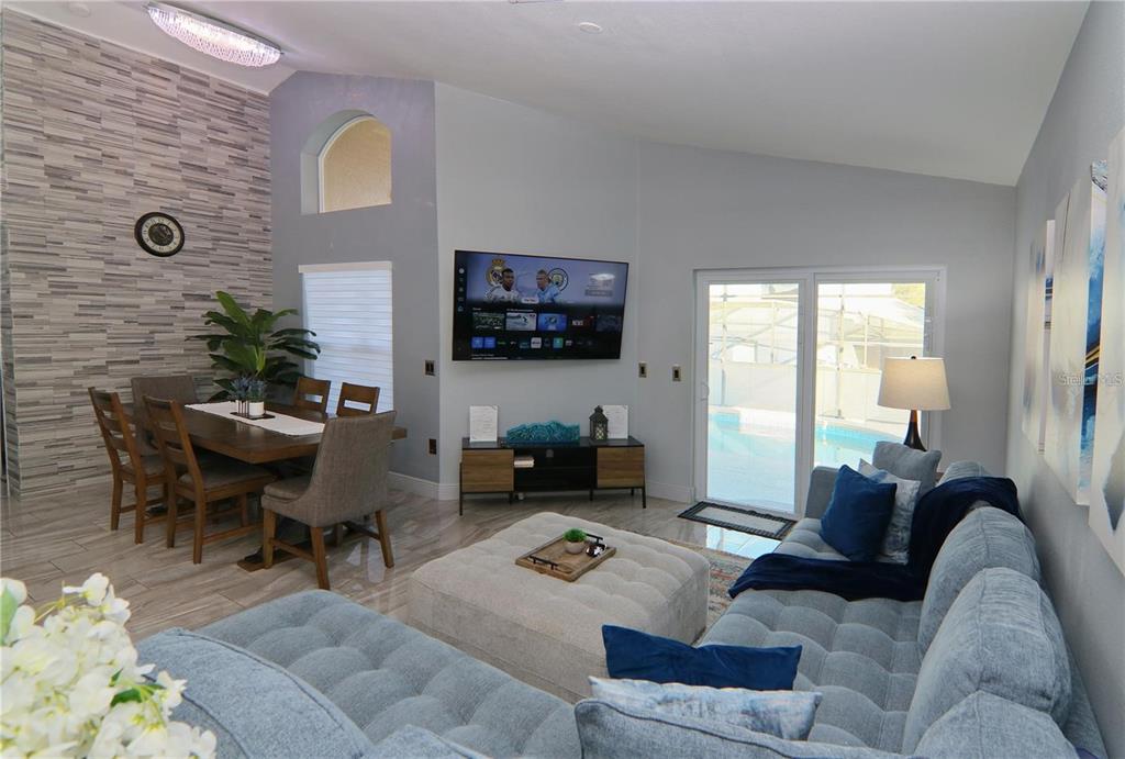 A living and dining area features a stone accent wall, tiled floors, and pool views — 1470 WEDGE WAY, HAINES CITY, FL