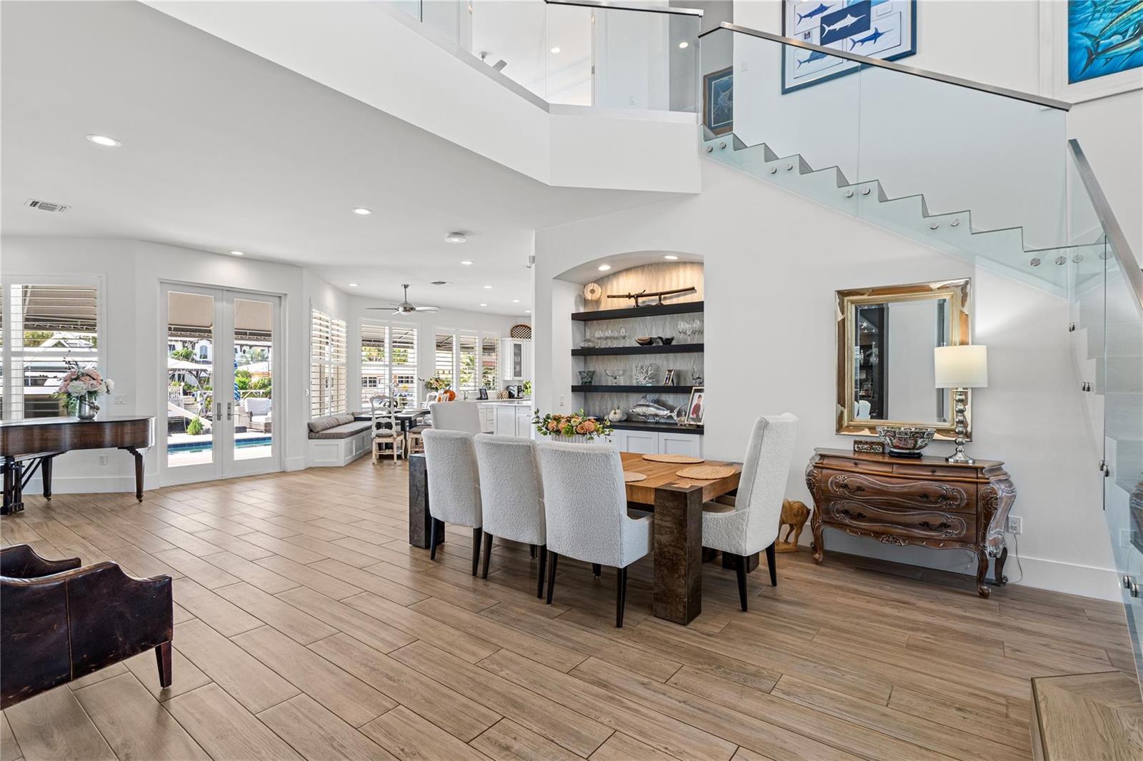 A dining area with a wooden table and chairs sits near a glass-railed staircase — 1580 SE 8th Street, Deerfield Beach FL 33441, DEERFIELD BEACH, FL