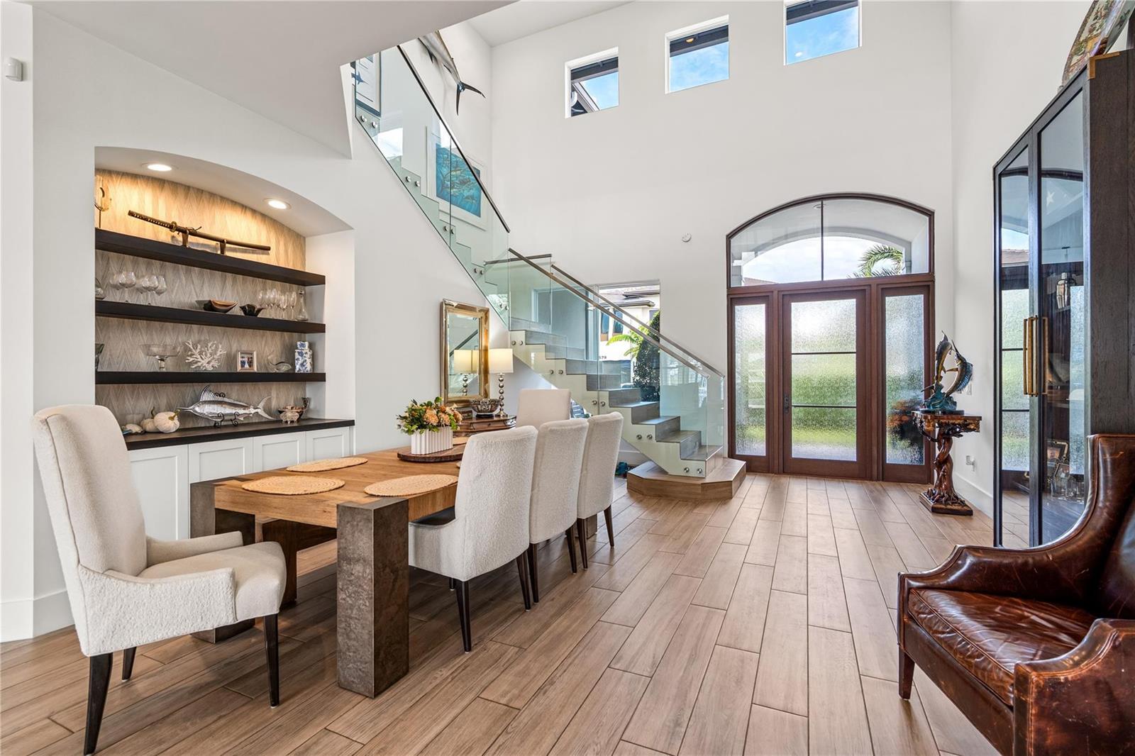 A dining room with a wooden table, glass-railed staircase, and high ceilings with windows — 1580 SE 8th Street, Deerfield Beach FL 33441, DEERFIELD BEACH, FL