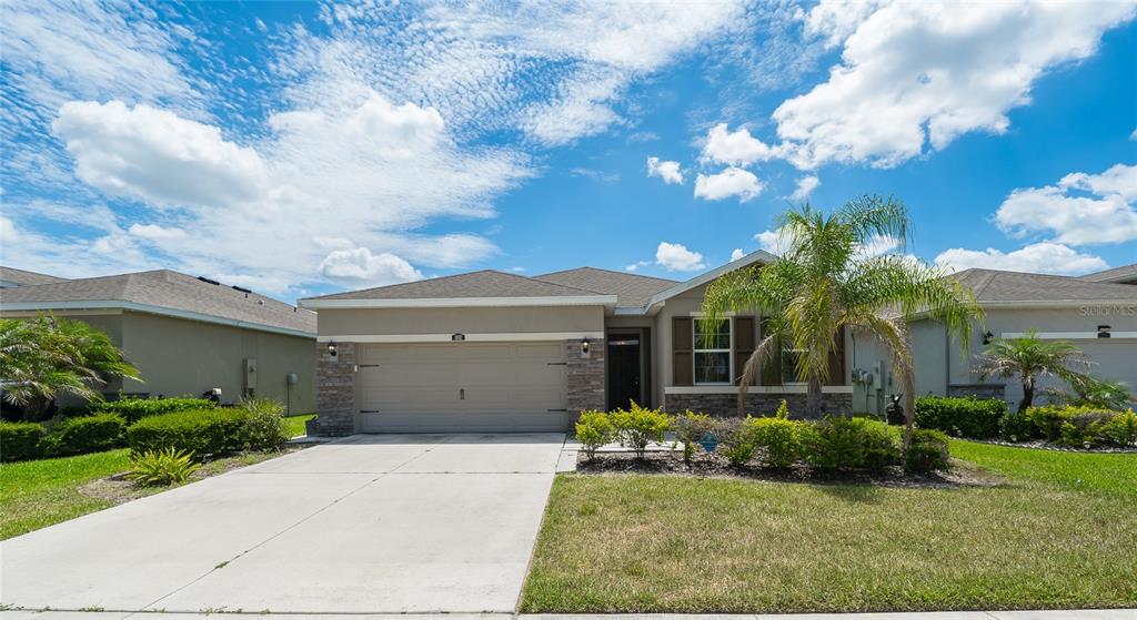 A single-story suburban house features a two-car garage, stone accents, and a front palm tree — 1092 PIPESTONE PLACE, WESLEY CHAPEL, FL
