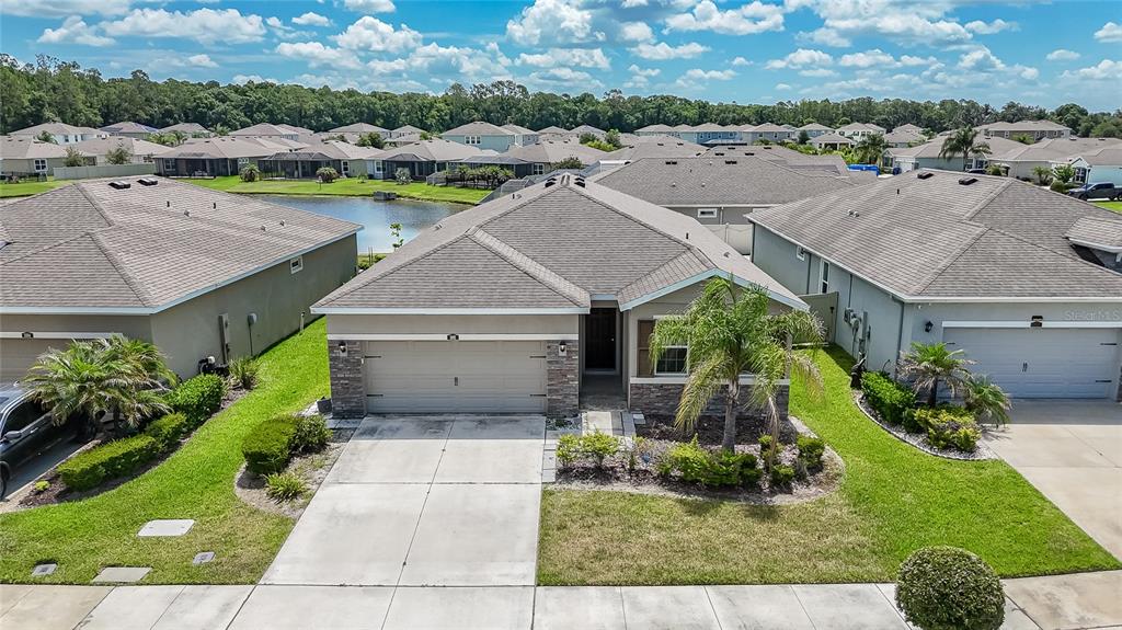 An aerial view shows a suburban house with a tan exterior, stone accents, and a driveway — 1092 PIPESTONE PLACE, WESLEY CHAPEL, FL