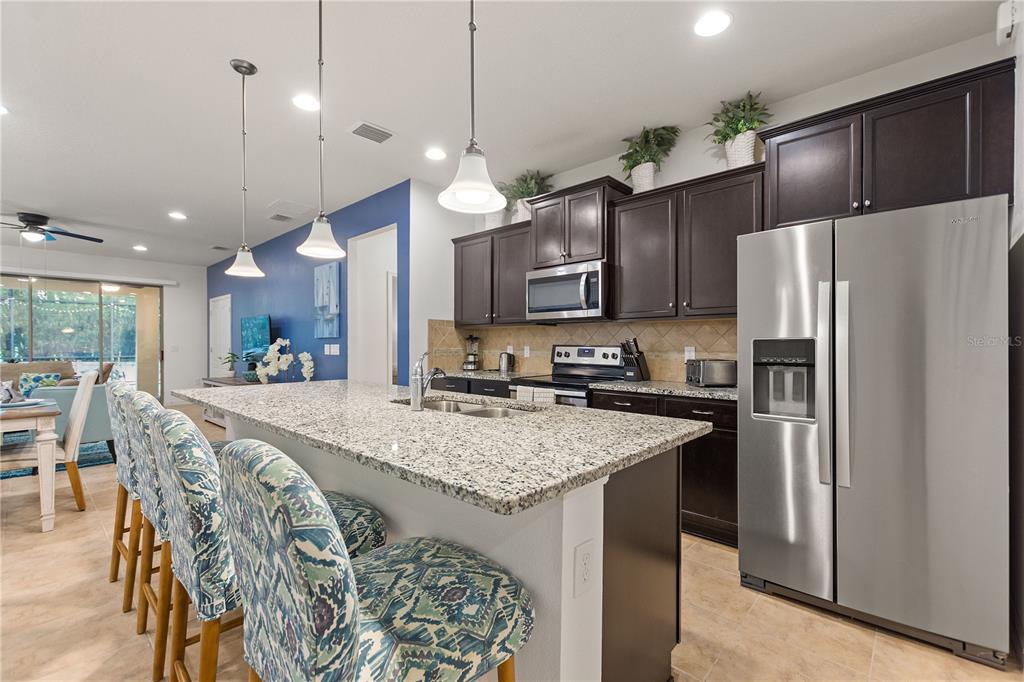 A kitchen features dark wood cabinets, granite countertops, a large island, and stainless steel appliances — 1861 NICE CT, KISSIMMEE, FL