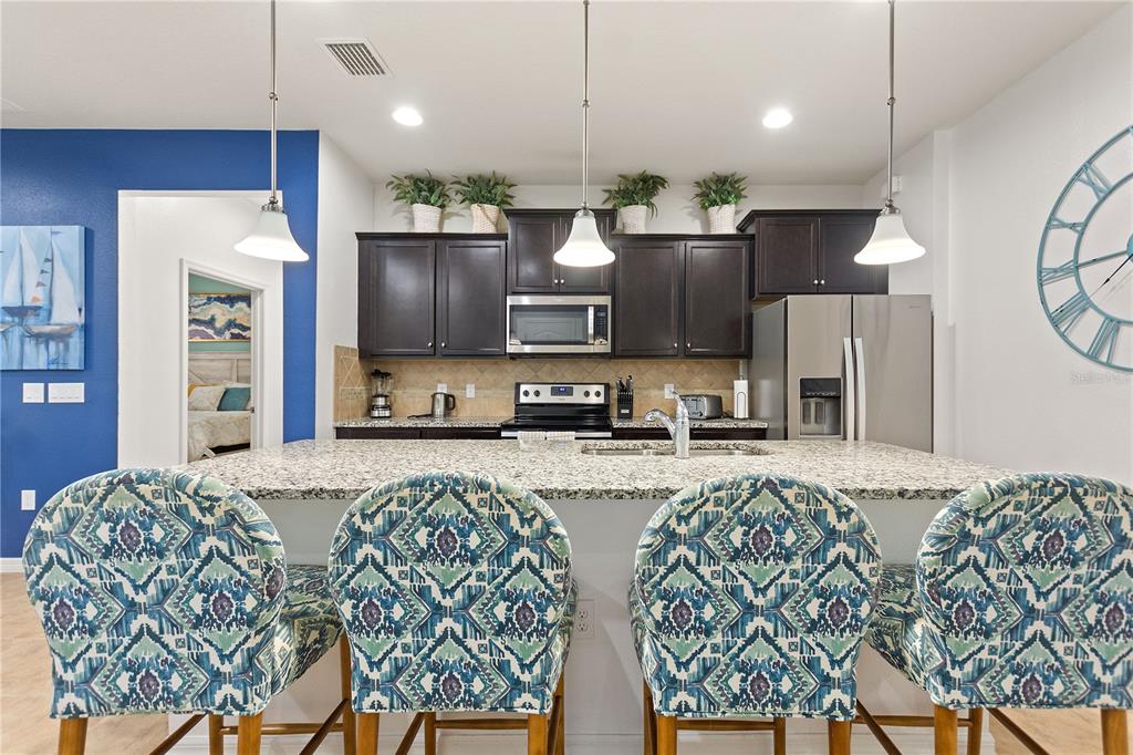 A kitchen features dark wood cabinets, granite countertops, a stainless steel refrigerator, and four patterned chairs — 1861 NICE CT, KISSIMMEE, FL