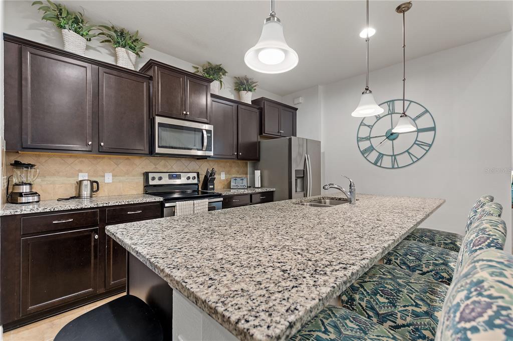 A kitchen features dark wood cabinets, granite countertops, a large island, and pendant lighting — 1861 NICE CT, KISSIMMEE, FL