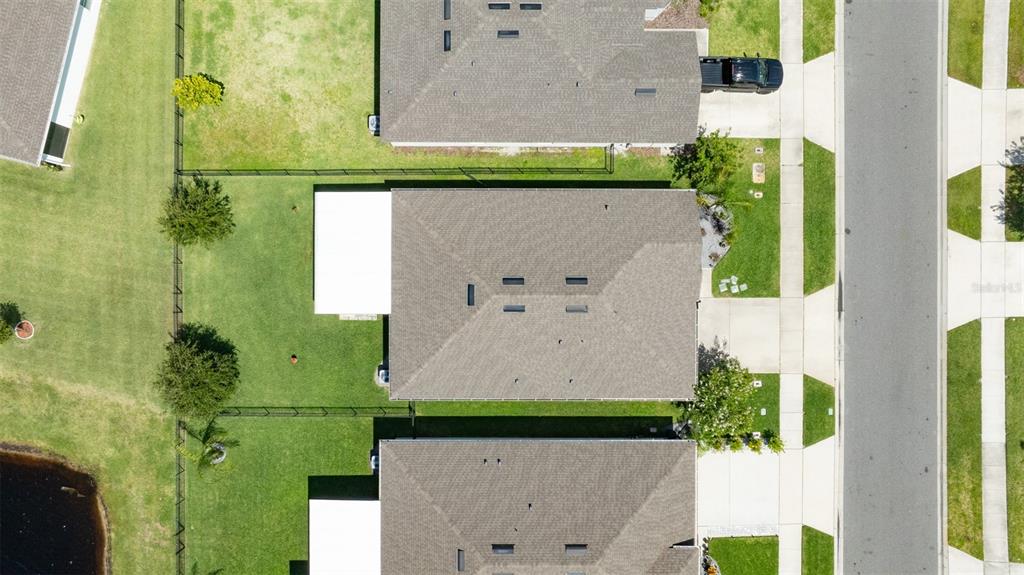 An aerial view shows three suburban houses with fenced backyards and a nearby pond — 2635 NEVERLAND DRIVE, NEW SMYRNA BEACH, FL