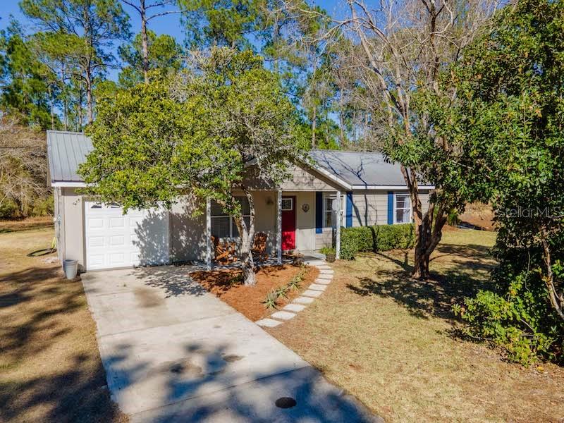 A single-story house with a metal roof, concrete driveway, and a red front door — 14641 NE 154TH STREET, FORT MC COY, FL