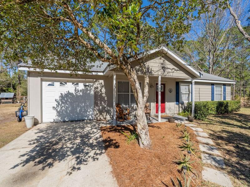 A single-story house with a white garage, red front door, and a large tree out front — 14641 NE 154TH STREET, FORT MC COY, FL